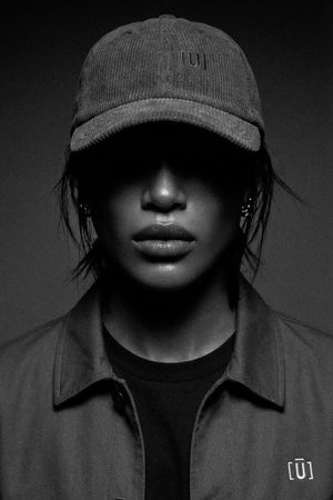 Person wearing a cap and dark clothing with a brand logo on a black background