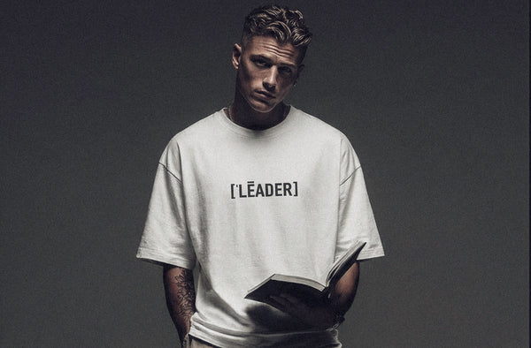 Model wearing ['LĒADER]™ t-shirt in light neutral color, clean studio background