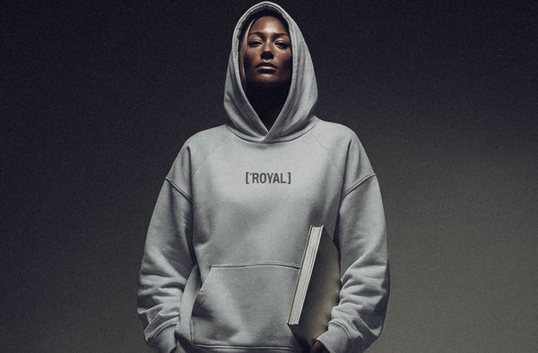 Model wearing ['ROYAL]™ hoodie in light neutral color, clean studio setting