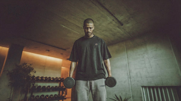 Man holding dumbbells in a dimly lit personal gym with dumbbell shelves in the background