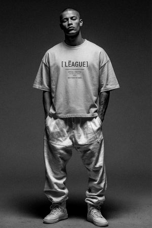 Person wearing a gray t-shirt with text and light-colored pants on a dark background