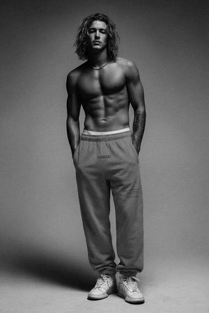 Man wearing beige sweatpants and white sneakers on a gray background
