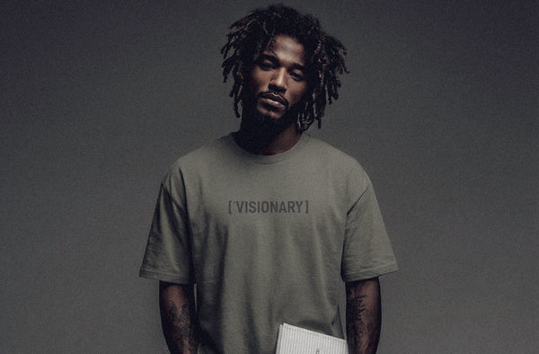 Model wearing ['VISIONARY]™ t-shirt in earth tone, minimal studio lighting